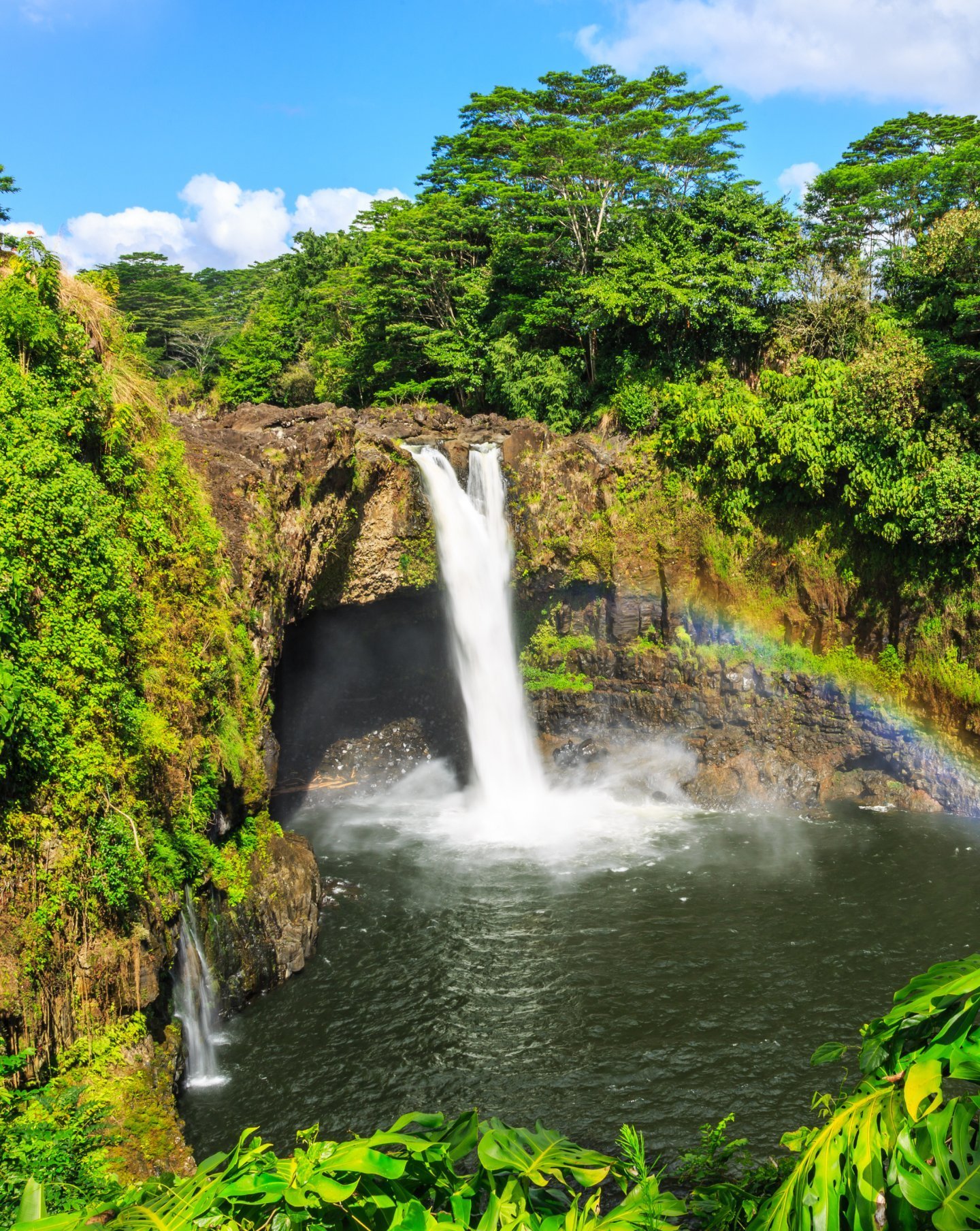 Waterfall in Hawaii with a rainbow surrounded by green trees